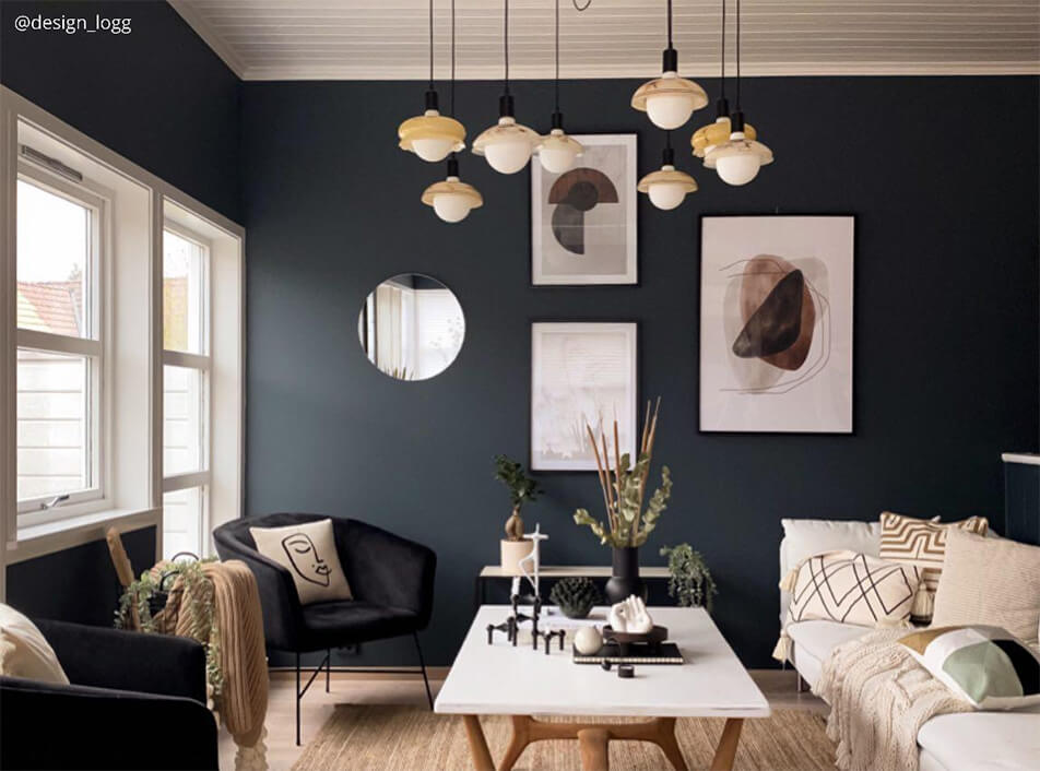 Obývačka s tmavými stenami, čiernymi sametovými kreslami, okrúhlym zrkadlom, grafickými plagátmi